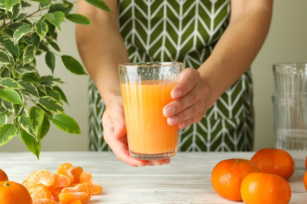 Mulher de avental segurando um copo com suco de tangerina, close-up