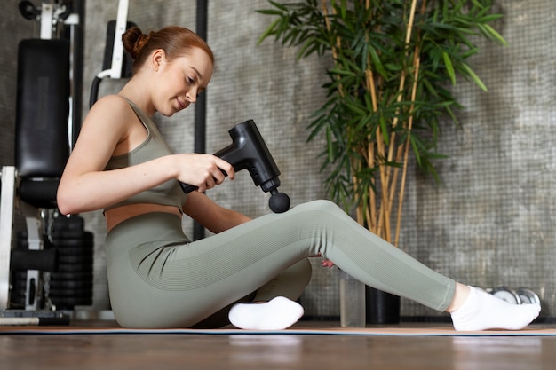 Foto mulher de baixo ângulo usando pistola de massagem na panturrilha