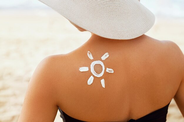 Mulher de beleza aplicando creme de creme solar no ombro bronzeado em forma de proteção solar