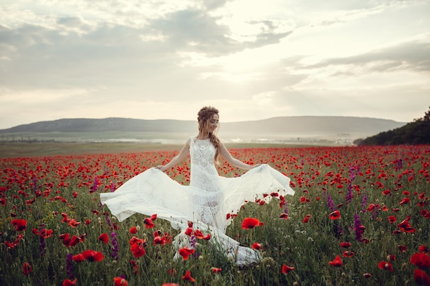 Mulher de beleza em campo de papoulas em vestido branco. Linda noiva no estilo Boho ao pôr do sol em um campo de papoulas vermelhas