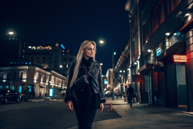 Mulher de beleza jovem sexy posando sobre fundo de rua iluminada cidade à noite. Férias de férias. Jovem loira elegante com cabelo comprido