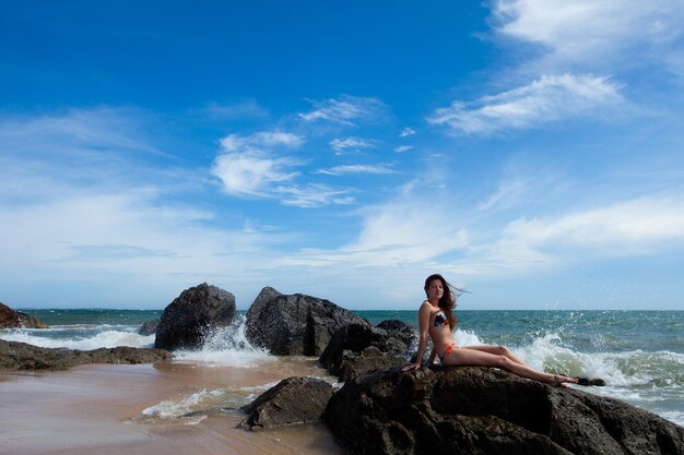 Mulher de beleza sentada na rocha no incrível oceano tropical