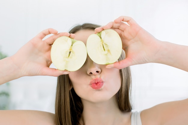 Mulher de beleza sorridente com metades de maçã com pele saudável no rosto posando sobre o fundo claro. Atraente vitamina fresca. Sessão de estúdio.