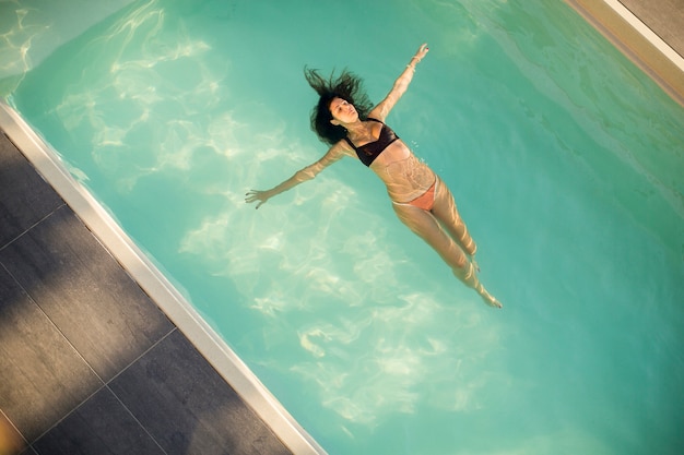 Mulher de biquíni flutuando na água na piscina no dia de verão