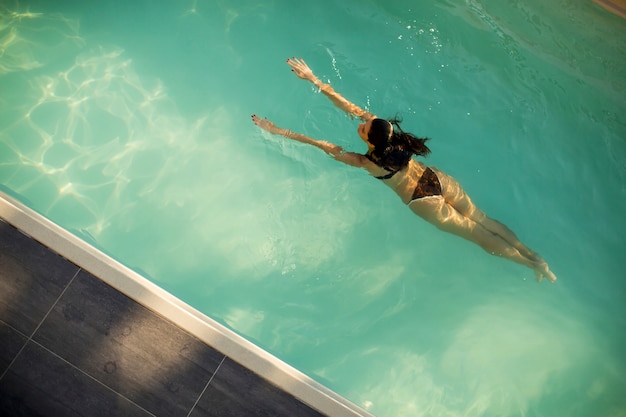 Mulher de biquíni flutuando na água na piscina no dia de verão