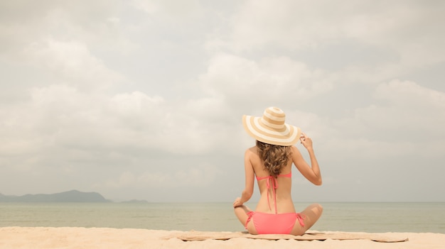 Mulher de biquíni rosa com chapéu de sol sentado na praia no verão