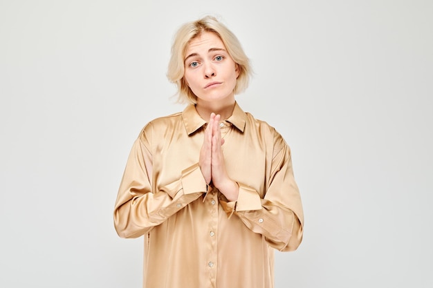 Foto mulher de blusa bege com expressão de súplica e mãos apertadas