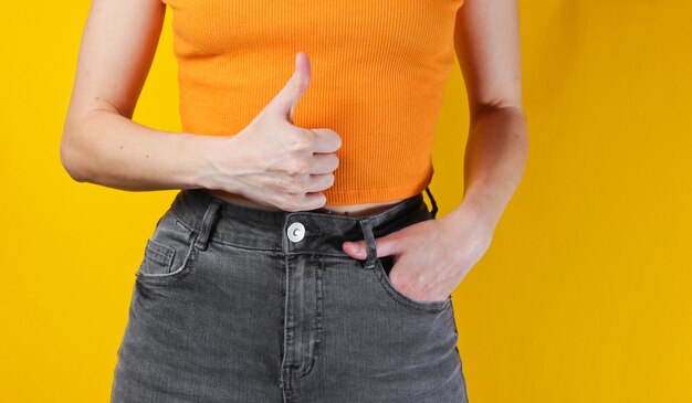 Mulher de blusa laranja e jeans mostrando os polegares para cima