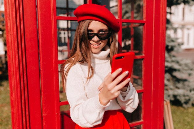 Mulher de boina vermelha com smartphone na rua