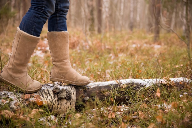 Mulher de botas quentes no velho tronco com primeira neve na floresta Caminhando no parque de inverno