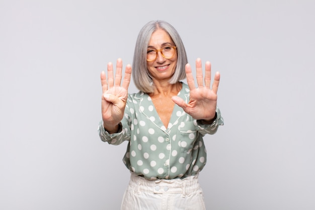 Mulher de cabelo grisalho sorrindo e parecendo amigável, mostrando o número nove ou nono com a mão para a frente, em contagem regressiva