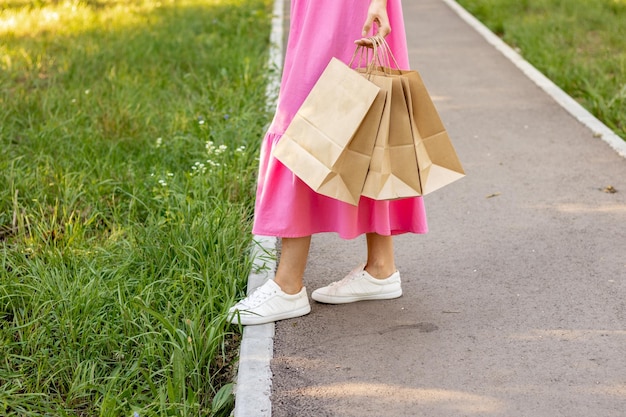 mulher de cabelo loiro lindo andando no parque com sacos de compras de papel marrom. garota de vestido rosa feliz