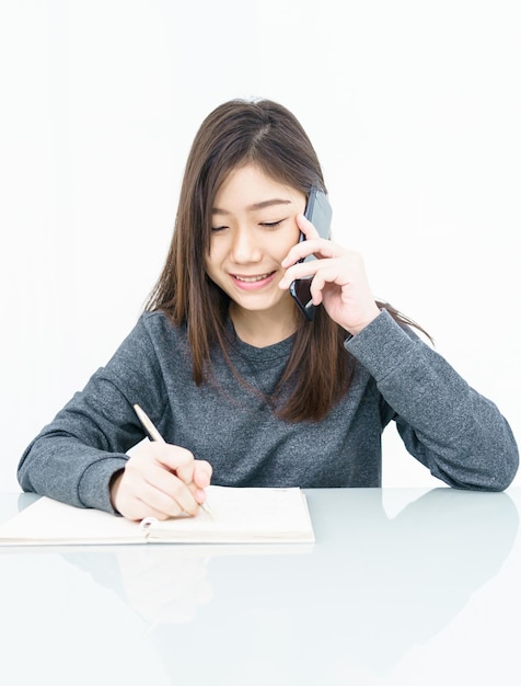 Foto mulher de cabelo longo mulher usando telefone celular e escrevendo um caderno em fundo branco