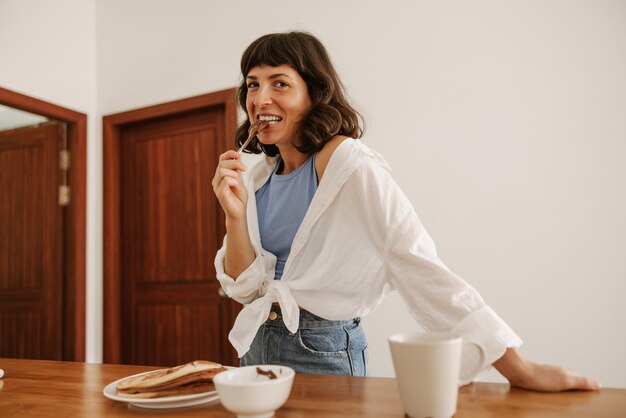 Mulher de cabelo morena de foto tenta chocolate na cozinha olhando para a câmera