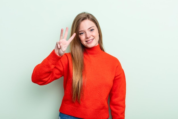 mulher de cabelo ruivo caucasiano sorrindo e parecendo amigável, mostrando o número três ou terceiro com a mão para a frente, em contagem regressiva