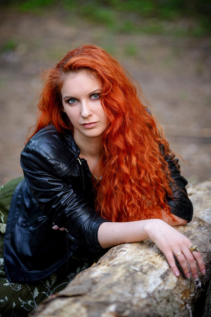 Foto mulher de cabelo vermelho sensual muito jovem moda sexy posando em uma superfície de floresta vestida com roupa de estilo rock moderno, jaqueta de couro.