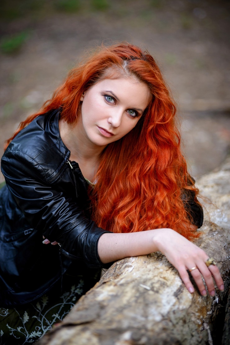 Foto mulher de cabelo vermelho sensual muito jovem moda sexy posando em uma superfície de floresta vestida com roupa de estilo rock moderno, jaqueta de couro.