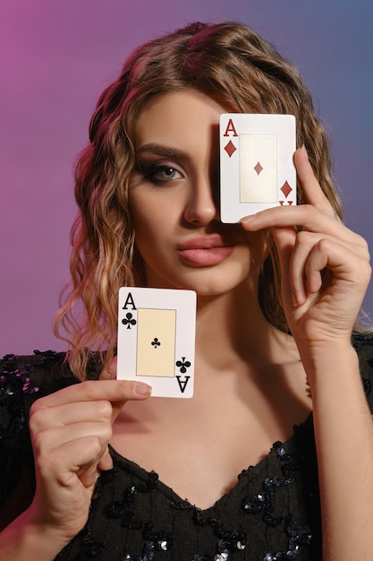Mulher de cabelos castanhos em um vestido preto brilhante mostrando duas cartas de jogar