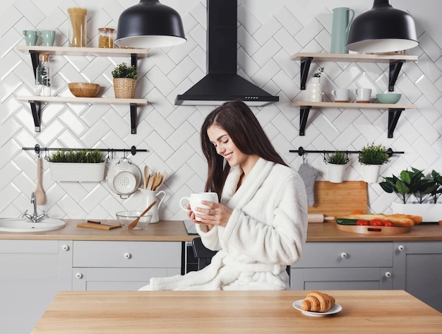 Mulher de cabelos compridos sentada com a xícara de café na cozinha moderna leve