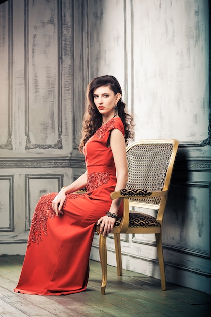 Mulher de cabelos escuros em um vestido de noite vermelho sentada em uma cadeira vintage