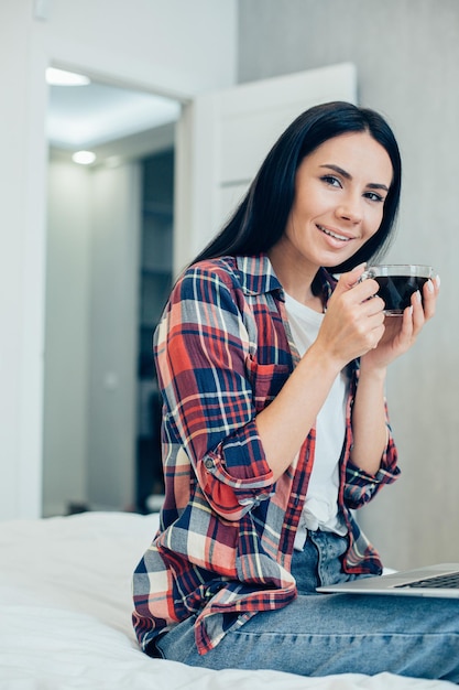 Mulher de cabelos escuros satisfeita em roupas casuais, parecendo satisfeita, segurando uma xícara de café preto nas mãos