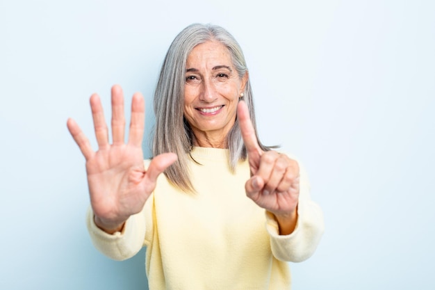 Mulher de cabelos grisalhos de meia-idade sorrindo e parecendo amigável, mostrando o número seis ou sexto com a mão para a frente, em contagem regressiva