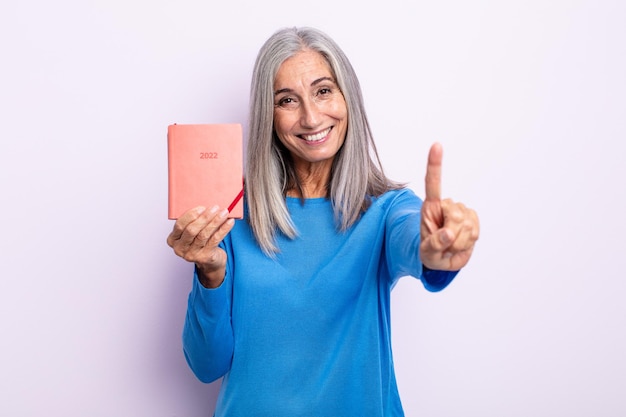 Mulher de cabelos grisalhos de meia-idade sorrindo e parecendo amigável, mostrando o número um. conceito de agenda 2022