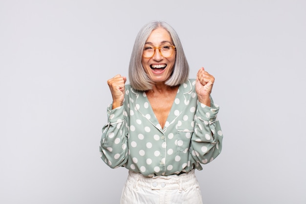Foto mulher de cabelos grisalhos se sentindo chocada, animada e feliz, rindo e comemorando o sucesso, dizendo uau!