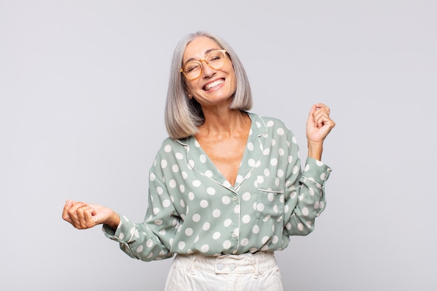 Mulher de cabelos grisalhos sorrindo, sentindo-se despreocupada, relaxada e feliz, dançando e ouvindo música, se divertindo em uma festa