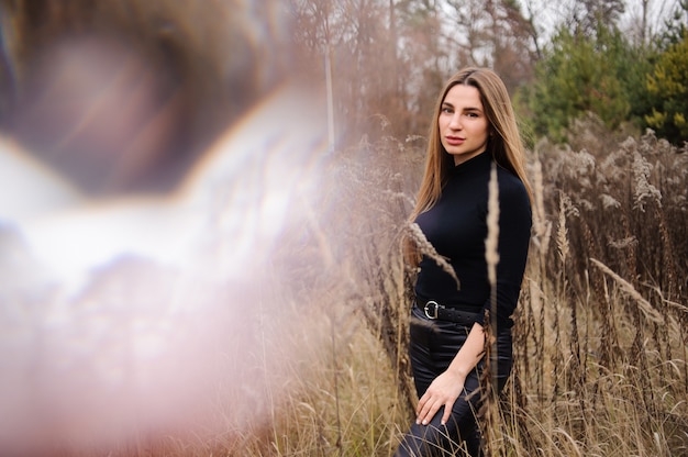 Foto mulher de calça preta e pé de blusa no campo de espigas secas