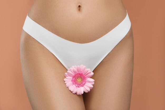 Mulher de calcinha branca com flor gerbera em closeup de fundo de pêssego