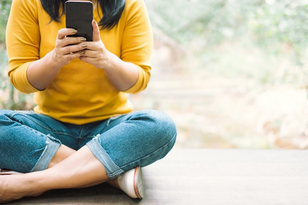 Mulher de camisa amarela, segurando um telefone móvel preto