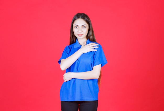 Mulher de camisa azul em pé na parede vermelha.