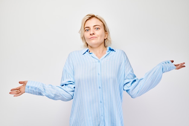 Mulher de camisa azul encolhendo os ombros com expressão brincalhona incerta em um fundo claro