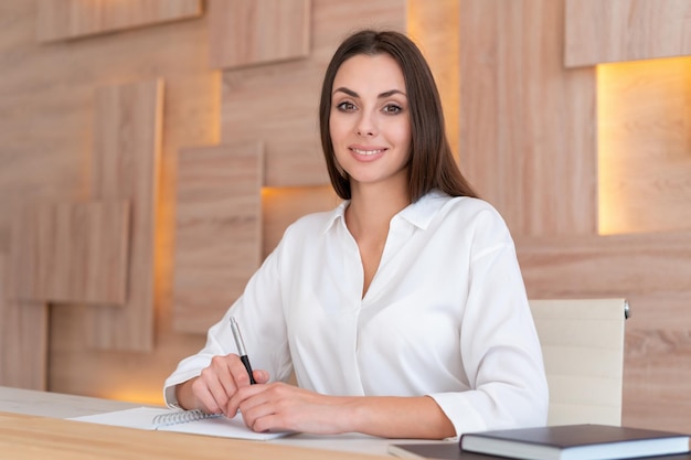 Mulher de camisa branca lindo sorriso sentado à mesa com notebook no interior do escritório de madeira