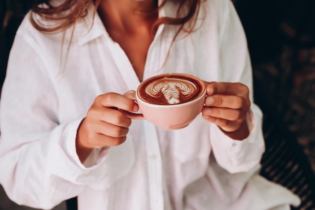 Mulher de camisa branca tomando cappuccino com latte art em um café