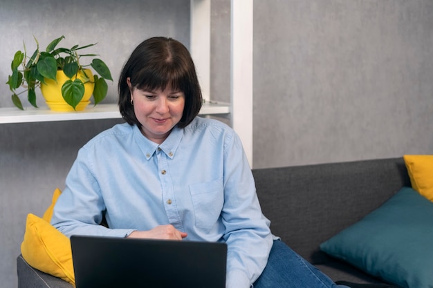 Mulher de camisa com laptop está trabalhando no sofá da sala. Mulher de negócios em processo de trabalho. Escritório em casa.