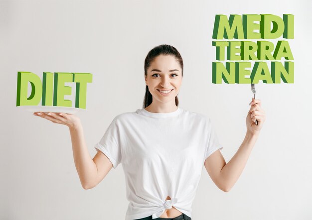 Mulher de camisa com o povo isolado no branco. Modelo feminino segurando um prato com letras da palavra Dieta, Mediterrâneo. Escolher uma alimentação saudável, dieta alimentar, nutrição orgânica e estilo de vida amigo da natureza.