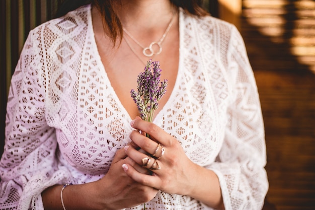 Mulher de camisa de crochê de renda branca, segurando um buquê de lavanda com colares de prata