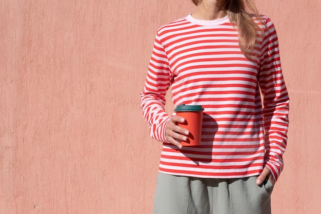 Mulher de camisa listrada segurando copo vermelho e bebendo café