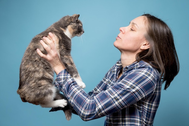 Mulher de camisa segura seu adorável gato nas mãos e olha para ela atentamente