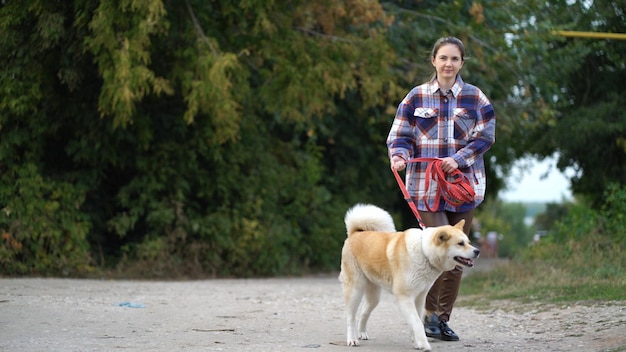 Foto mulher de camisa xadrez segurando cachorro akita inu na coleira vermelha enquanto caminhava ao ar livre