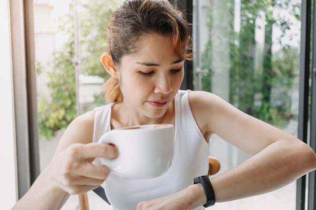 Mulher de camiseta branca bebendo café e olhando para o relógio