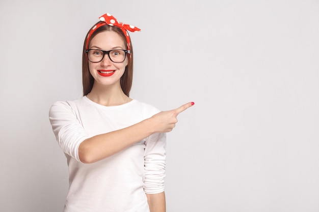 Mulher de camiseta branca com sardas, óculos, lábios vermelhos e faixa na cabeça