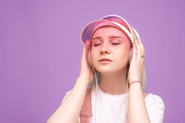 Mulher de camiseta branca e boné rosa ouve música com fones de ouvido