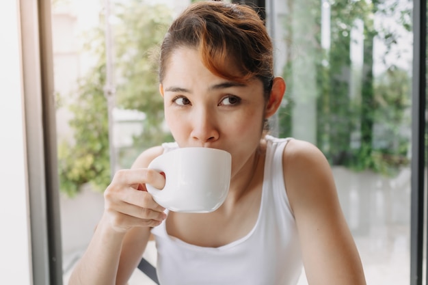 Mulher de camiseta branca está bebendo uma bebida quente no copo