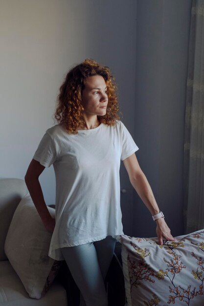 Mulher de camiseta branca olha para a janela Foto de alta qualidade