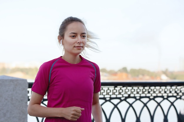 Mulher de camiseta corre ao longo da cerca na cidade no verão