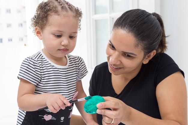 Mulher de camiseta preta com bebê pintando ovo de Páscoa.