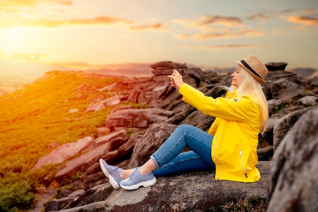 Mulher de casaco amarelo chegando ao destino e no topo da montanha e tirando selfie